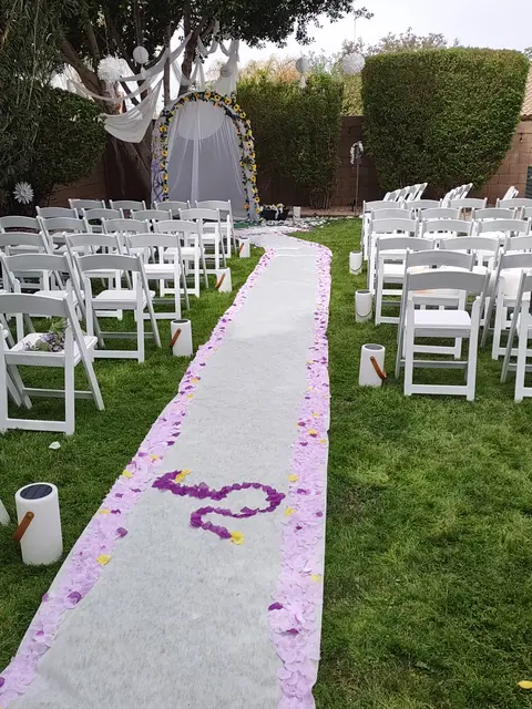 Backyard wedding aisle with white chairs and floral arch